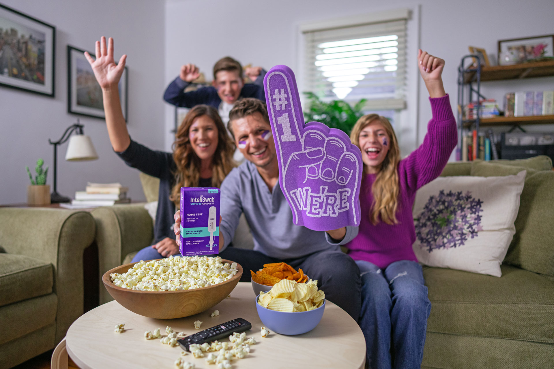 A family holds a We're #1 foam hand and a box of InteliSwab while celebrating in their living room.