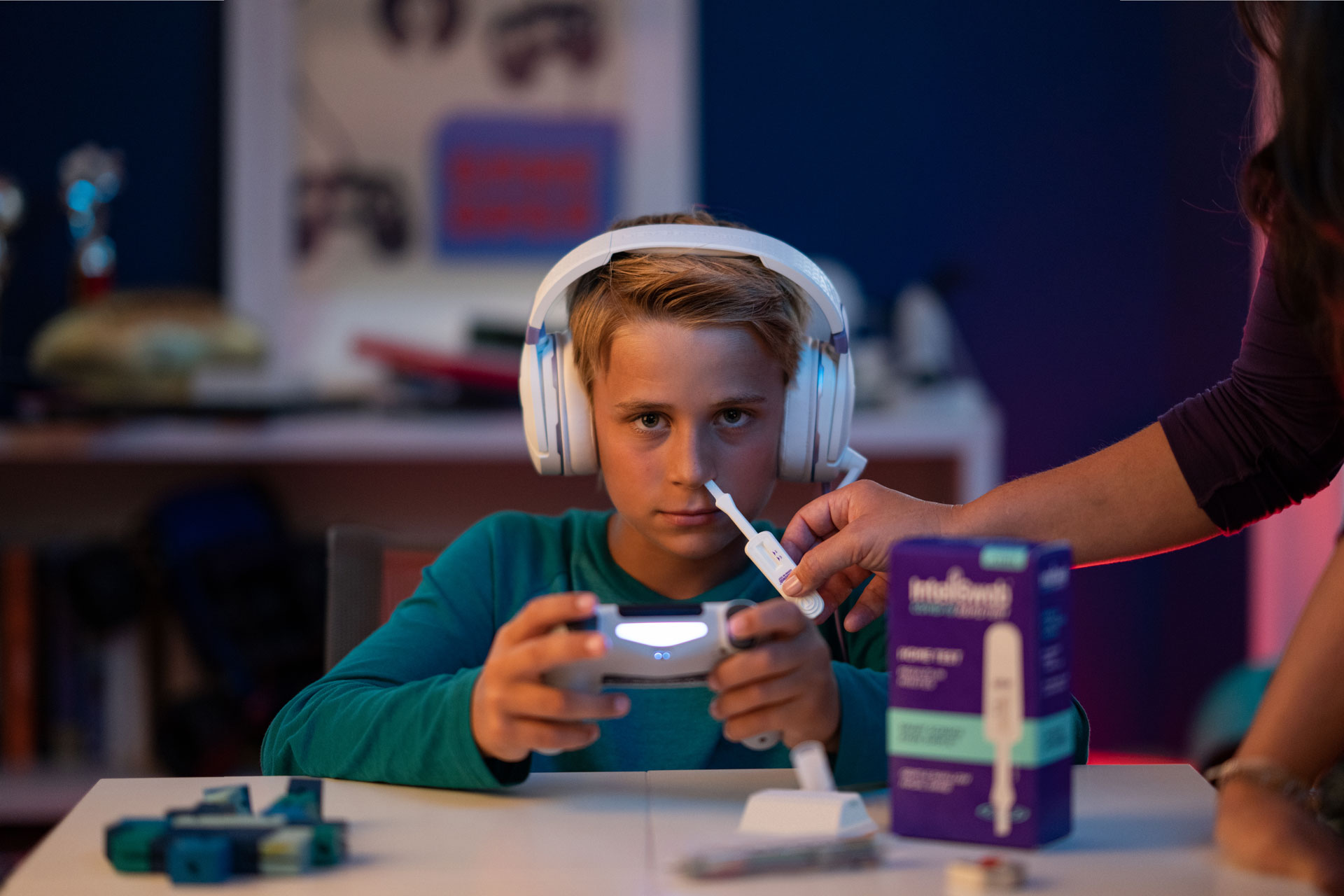 A boy plays a video game while getting his nose swabbed.