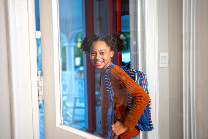 A schoolgirl smiles at the camera while heading out the door.