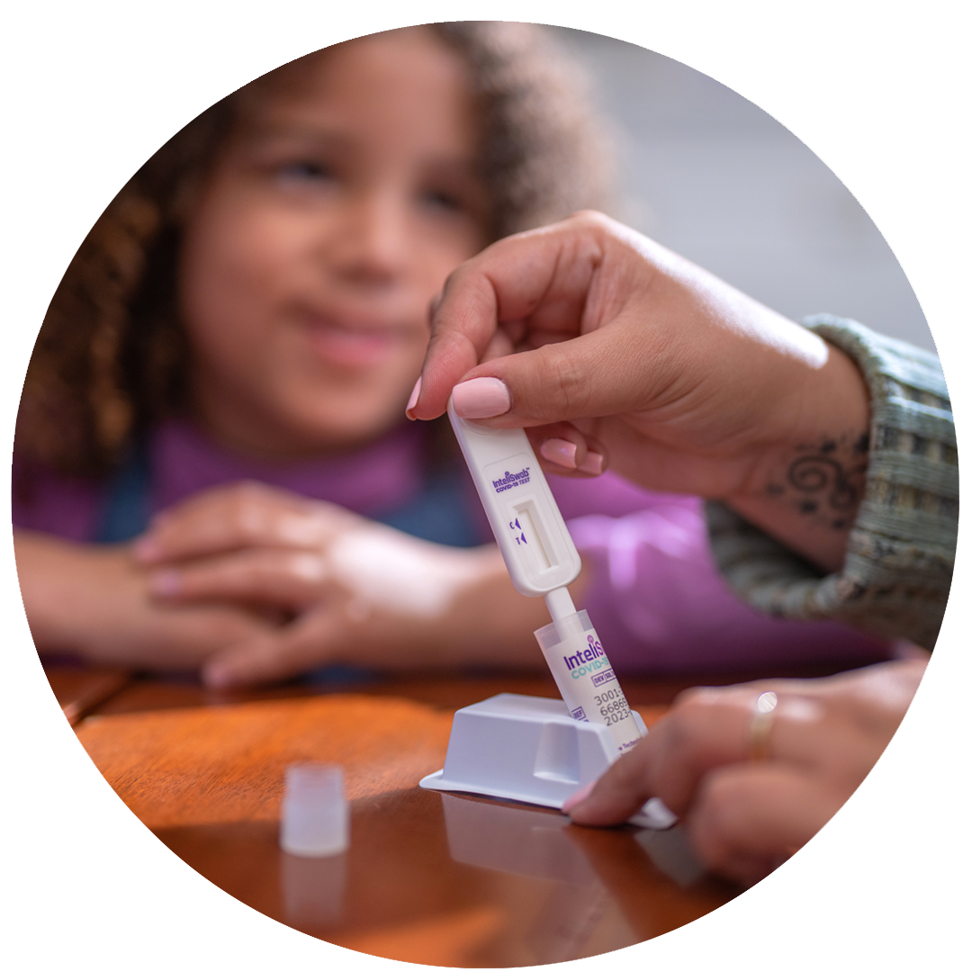 A woman's hand swirls the swab in a tube of fluid while a young girl looks on smiling.