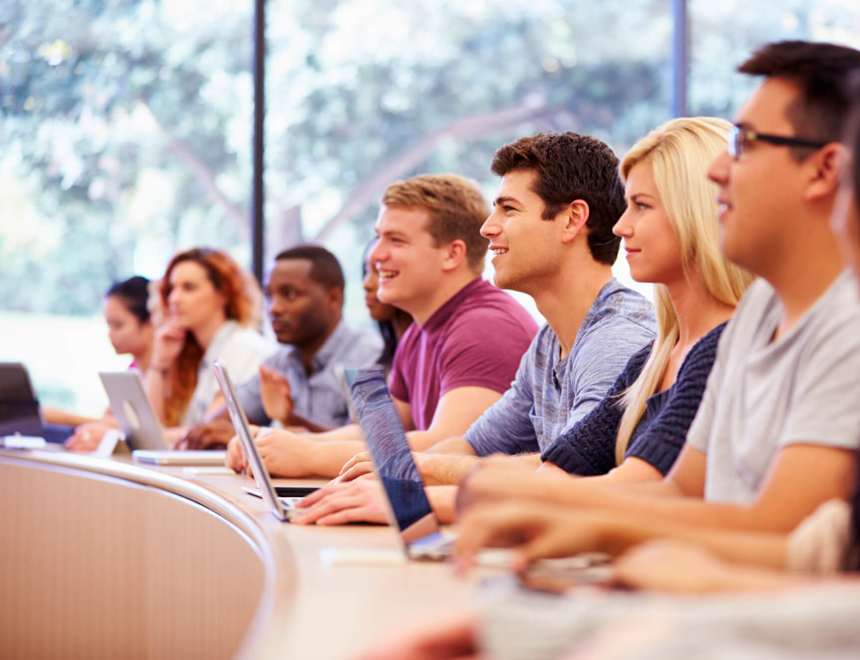 A group of college students sits in a row listening intently and taking notes.