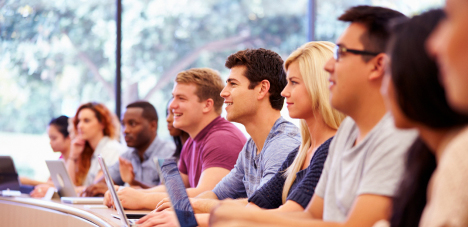 A group of college students sits in a row taking notes.